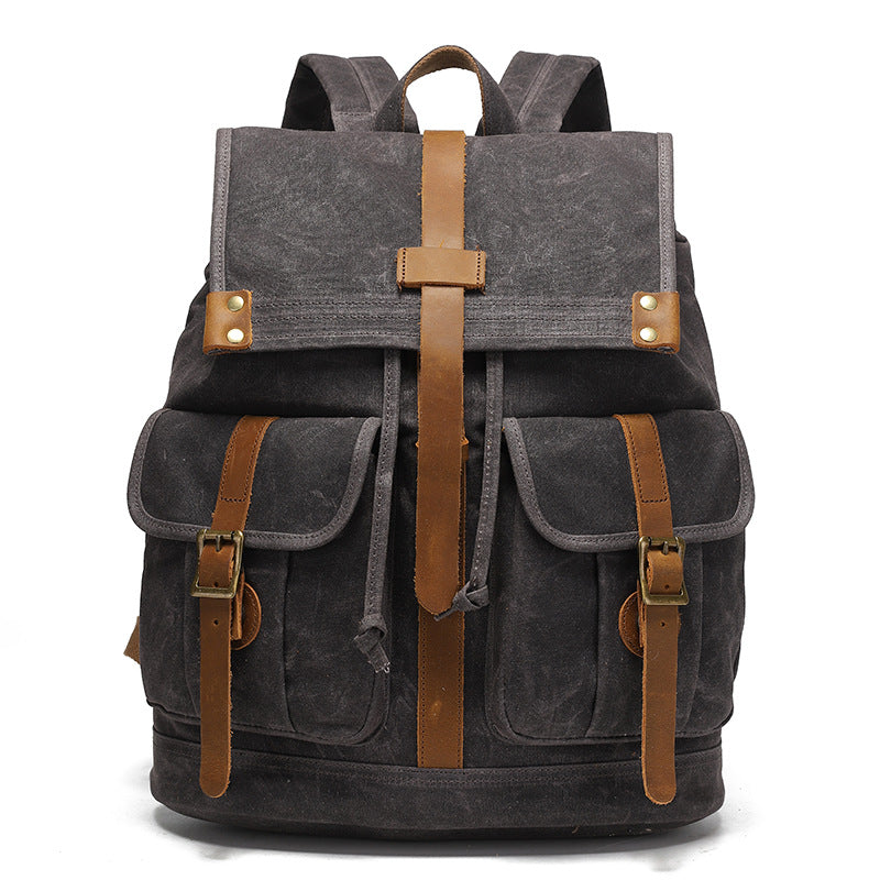Vintage Waxed Canvas Rucksack Backpack - Front view of the dark charcoal gray version, with signature waxed canvas material, brown leather straps, and brass buckle details.