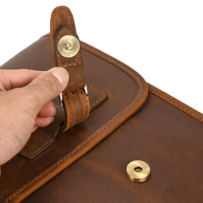 Brown leather bag with gold rivets and a hand holding the strap against a white background
