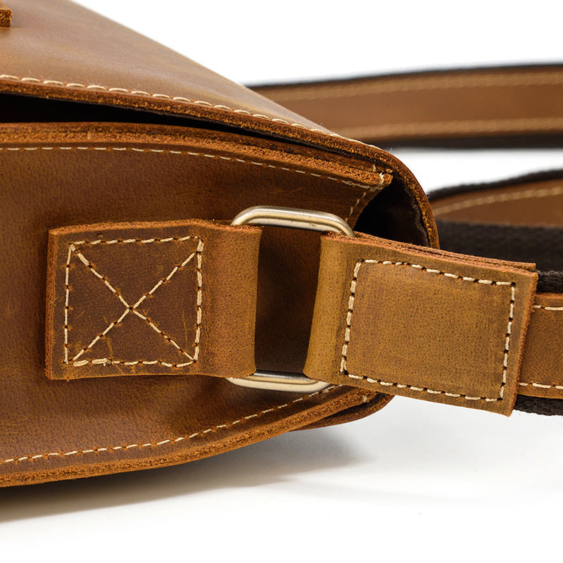 Close-up of a brown leather bag with a strap and stitching detail on a white background