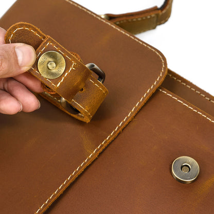 Brown leather bag with gold rivets and a hand holding a strap.