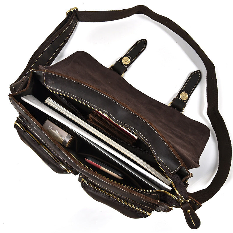 Brown leather bag with a shoulder strap, open to reveal a laptop inside, on a white background.