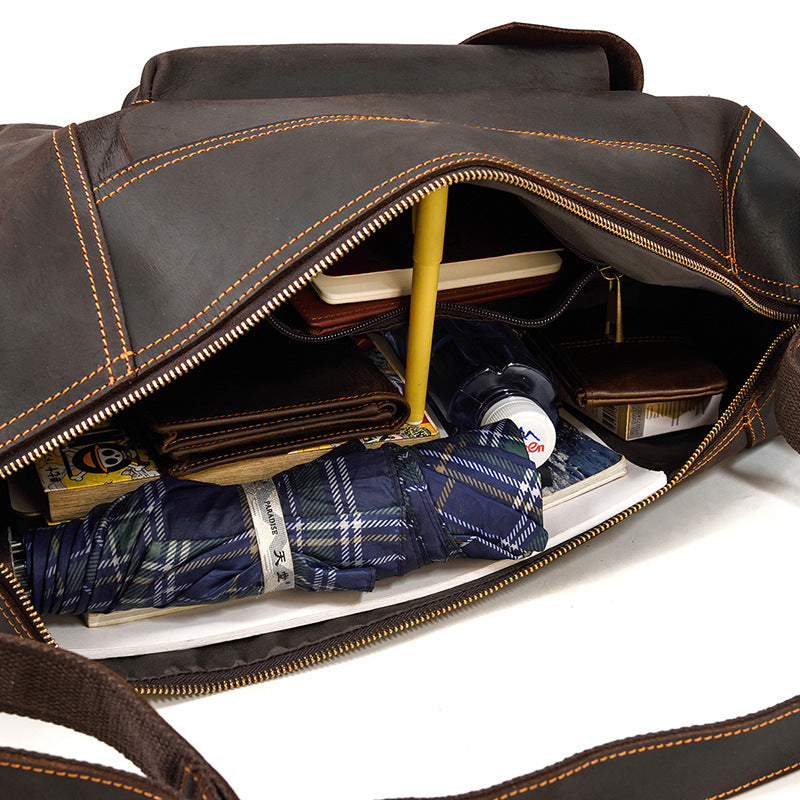 Brown leather bag with items like a shirt, wallet, and books inside on a white background