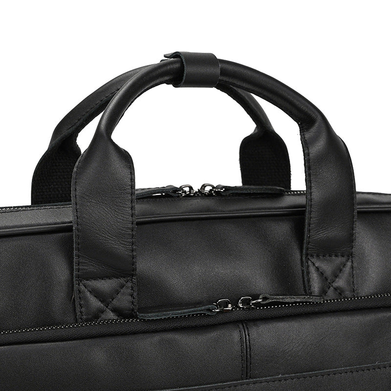 Close-up of a black leather briefcase with handles and zippers.