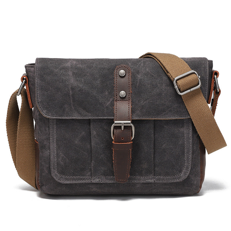 Vintage charcoal grey waxed canvas messenger bag with brown leather strap detail, front view.